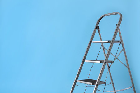 Metal stepladder on light blue background, space for text. construction equipmentの写真素材