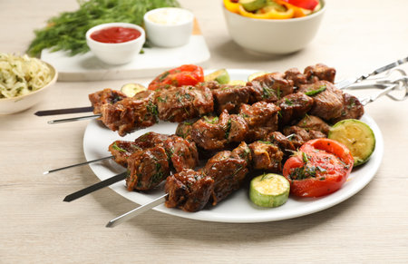 Metal skewers with delicious meat and vegetables served on white wooden tableの写真素材