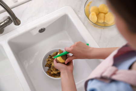 Woman peeling potato near kitchen sink, closeup. Preparing vegetablesの写真素材
