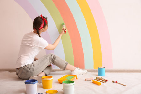 Young woman painting rainbow on white wall indoorsの写真素材