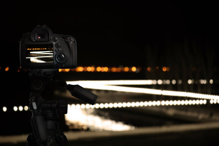 Taking photo of camera mounted on tripod. Blurred view of city lights at night, bokeh effectの写真素材