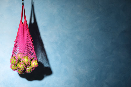 Mesh bag with ripe apples hanging on light blue background. Space for textの写真素材