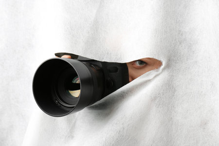 Hidden woman with camera spying through hole in white fabricの写真素材