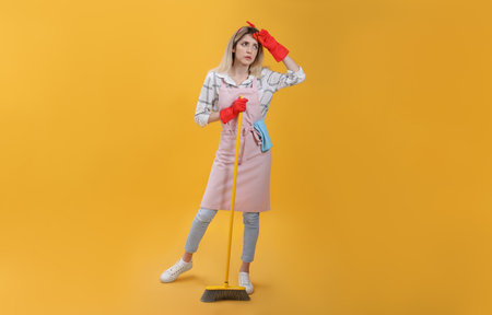 Young housewife with broom on yellow backgroundの写真素材