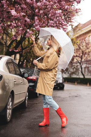 Young woman with umbrella near blossoming tree on spring dayの写真素材
