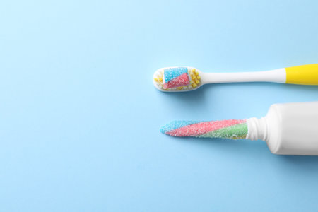 Toothpaste tube and brush with gummy candies on light blue background, flat lay. Dangers of sugarの写真素材