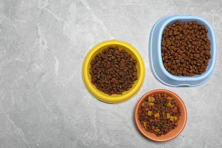 Pet bowls with dry food on light gray background, flat lay. Space for textの写真素材
