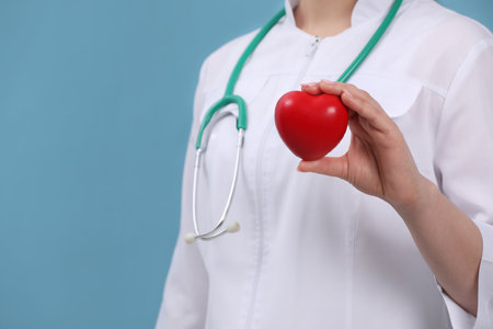 Doctor holding red heart on light blue background, closeup. Space for textの写真素材