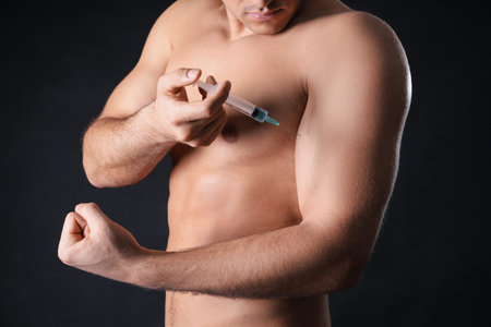 Athletic man injecting himself on black background, closeup. Doping conceptの写真素材