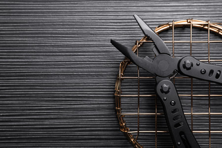 Modern compact portable multitool on black wooden table, top view. Space for text