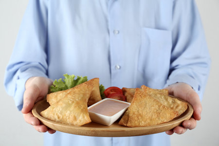 Woman holding plate with delicious samosas and sauce on light gray background, closeupの写真素材