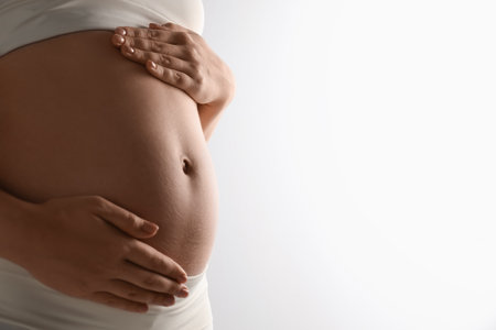 Pregnant young woman touching belly on light background, closeup. Space for textの写真素材