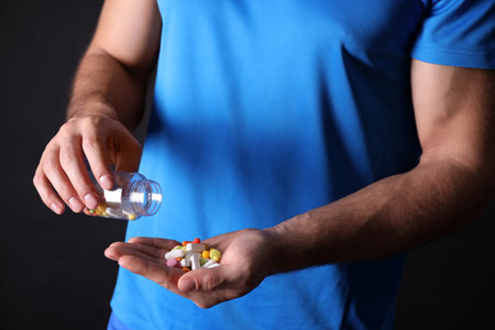 Man with bottle of pills on black background, closeup. Doping conceptの写真素材