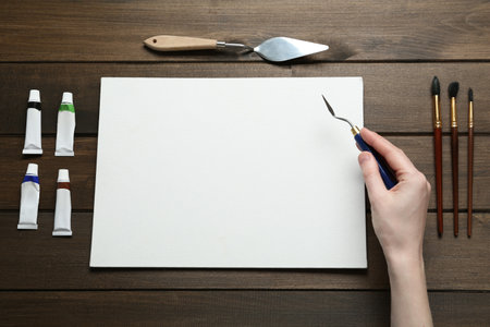 Man with spatula and blank canvas on wooden table, top viewの写真素材