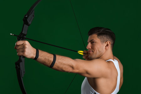 Man with bow and arrow practicing archery on green backgroundの写真素材