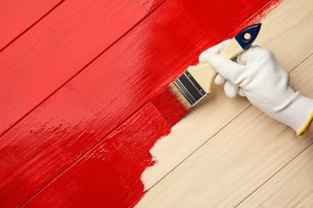 Worker in gloves painting wooden surface with red dye, top view. Space for textの写真素材