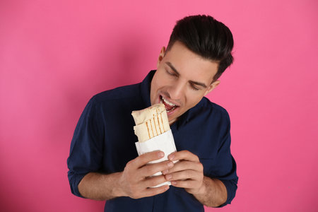 Man eating delicious shawarma on pink backgroundの写真素材