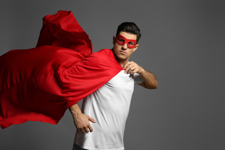 Man wearing superhero cape and mask on gray backgroundの写真素材