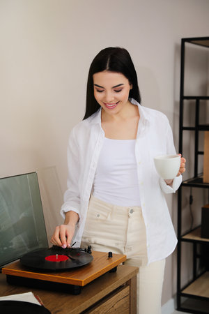 Happy young woman using turntable at homeの写真素材