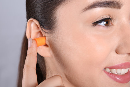 Young woman inserting foam ear plug on grey background, closeupの写真素材