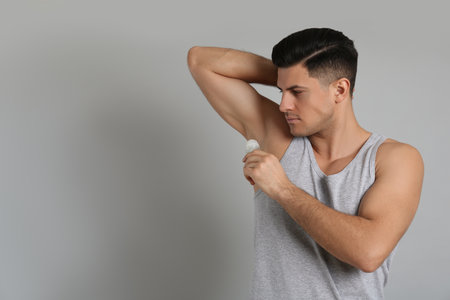 Handsome man applying deodorant to armpit on gray background, space for textの写真素材