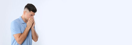 Man with tissue suffering from runny nose on white backgroundの写真素材