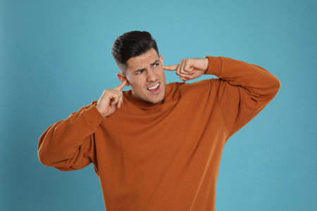 Emotional man covering ears with fingers on light blue backgroundの写真素材