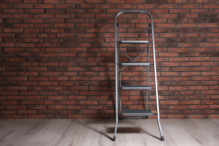 Modern metal stepladder near brick wall indoors. Space for textの写真素材