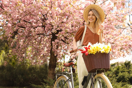 Beautiful young woman with bicycle and flowers in park on pleasant spring day. Space for textの写真素材