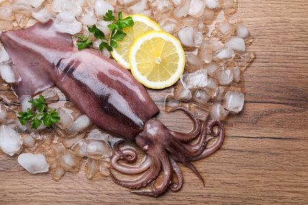Fresh raw squid with ice, lemon and parsley on wooden table, flat layの写真素材