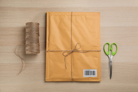 Padded envelope, rope and scissors on wooden background, flat lay