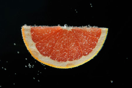 Slice of grapefruit in sparkling water on black background. Citrus sodaの写真素材