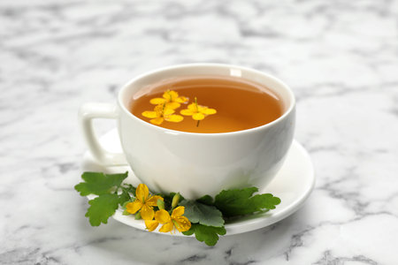Cup of aromatic celandine tea and flowers on white marble table, closeupの写真素材
