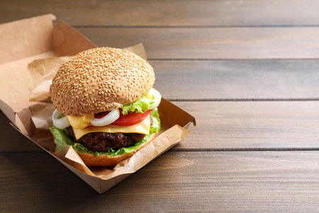 Delicious burger in cardboard box on wooden table. Space for textの写真素材