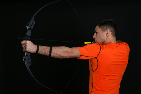 Man with bow and arrow practicing archery on black backgroundの写真素材