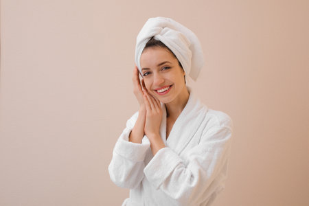 Beautiful young woman with hair wrapped in towel after washing on beige backgroundの写真素材