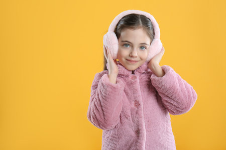 Cute girl wearing stylish earmuffs on yellow background. Space for textの写真素材