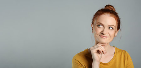Portrait of thoughtful red haired woman with charming smile on gray backgroundの写真素材