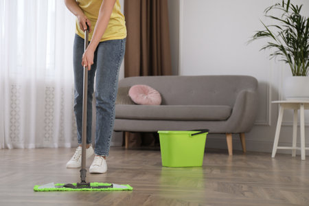 Woman cleaning floor with mop in living room, closeup