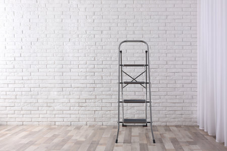 Modern metal stepladder near white brick wall indoors. Space for textの写真素材