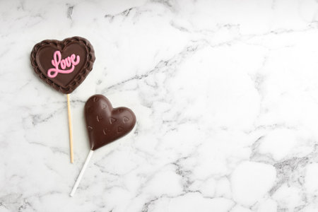 Different chocolate heart shaped lollipops on white marble table, flat lay. Space for textの写真素材