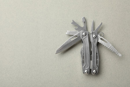 Compact portable metallic multitool on light gray background, top view. Space for text
