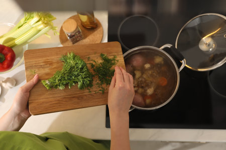 Woman putting dill into pot to make bouillon in kitchen, top view. homemade recipeの写真素材