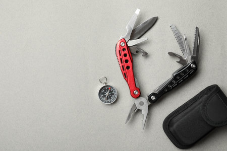 Compact portable multitool, case and compass on light gray background, flat lay. Space for text