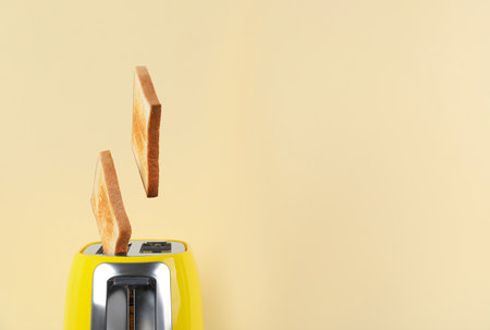 Bread slices popping up from modern toaster on beige background, closeup. Space for textの写真素材