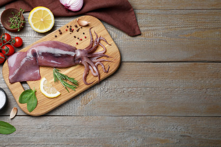 Flat lay composition with fresh raw squid and garnish ingredients on wooden table. Space for textの写真素材