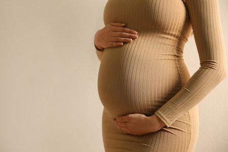 Pregnant woman touching her belly on beige background, closeup. Space for textの写真素材