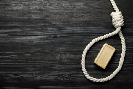 Rope noose and soap bar on dark wooden table, flat lay. Space for textの写真素材