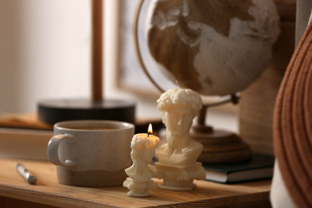 Beautiful David bust candles and cup of hot drink on table indoors, space for textの写真素材