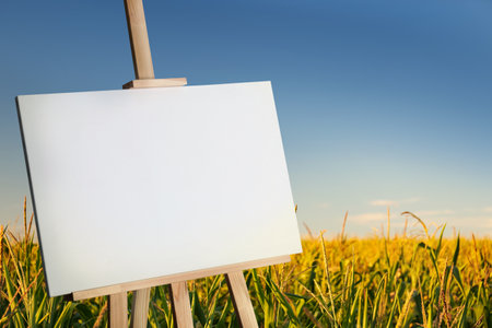 Wooden easel with blank canvas in corn field on sunny day. Space for textの写真素材